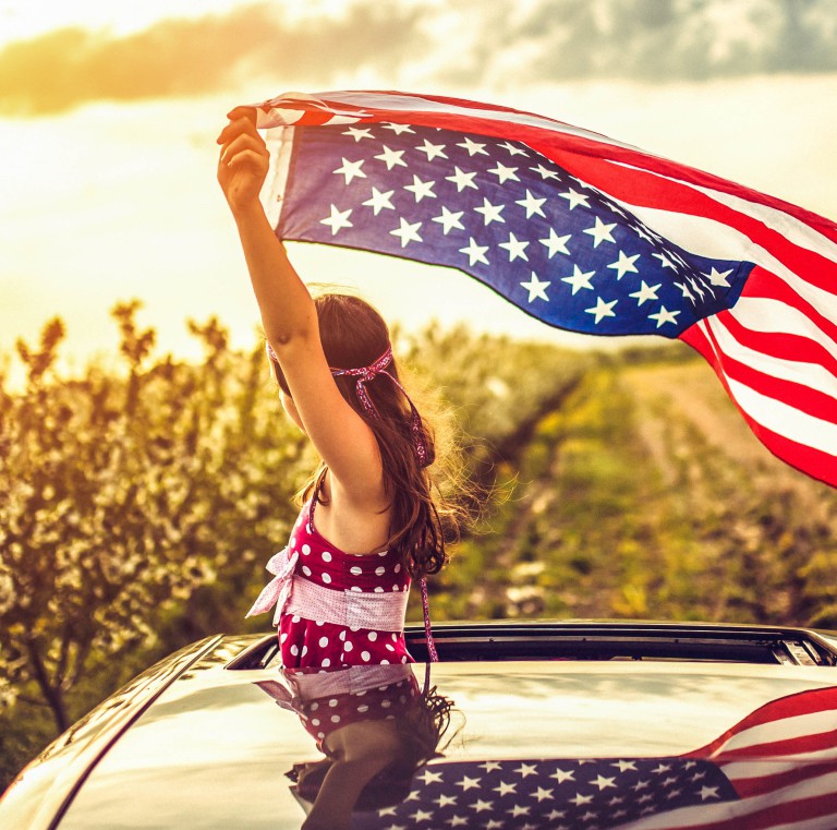 Girl Through a Car Sunroof Waving with USA Flag