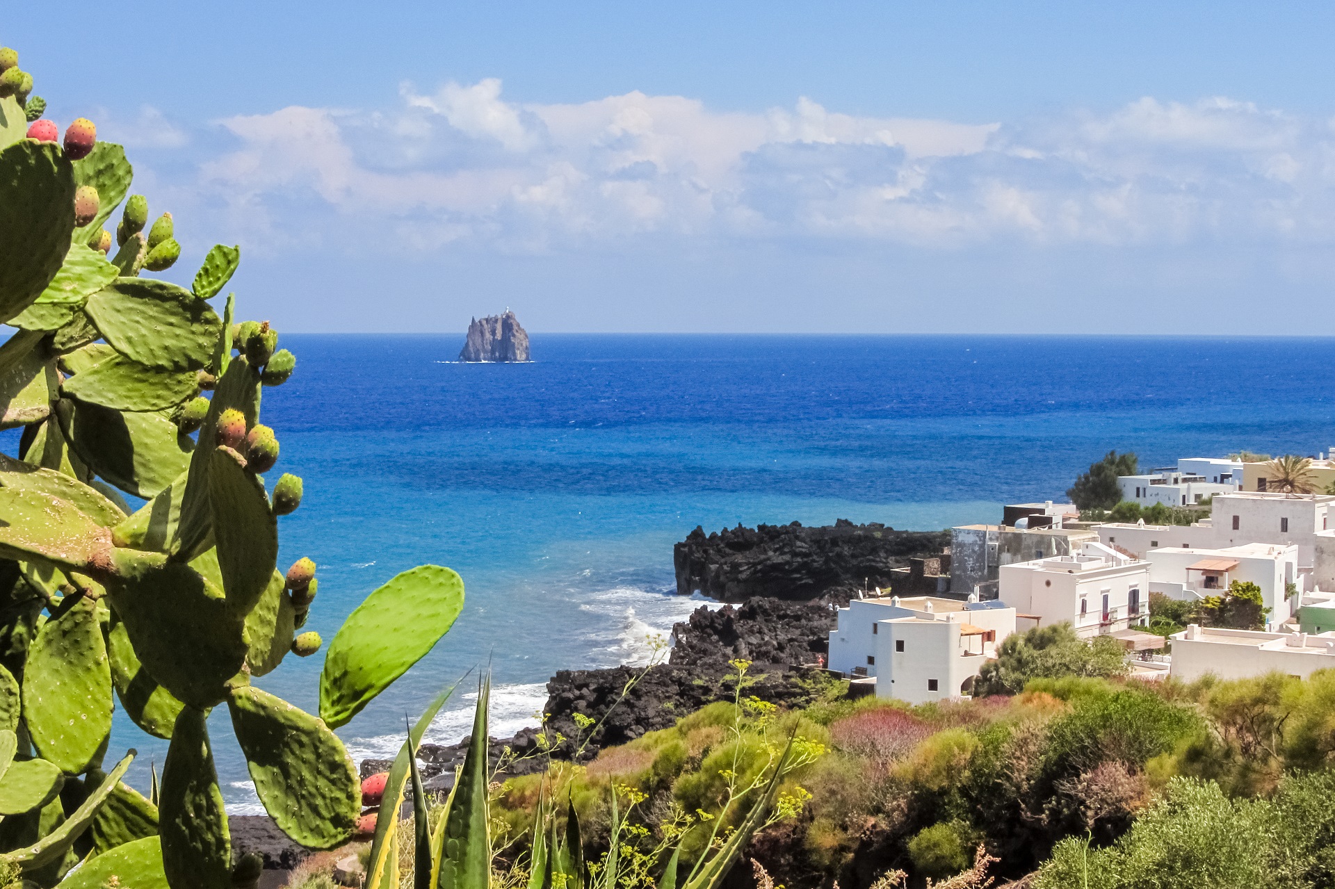 Die Küste der Insel Stromboli ist geprägt vom Kontrast zwischen schwarzem Vulkangestein, weißen Häusern und dem türkisen Meer.
